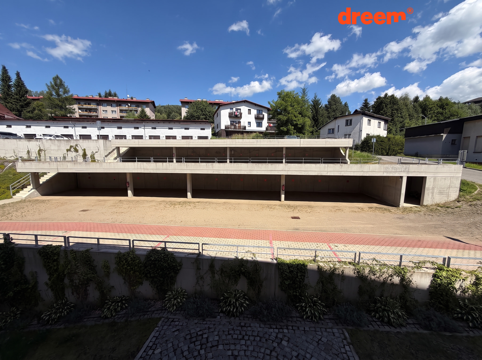Pohled na dvoupodlažní betonovou konstrukci s krytými parkovacími místy za slunečného dne