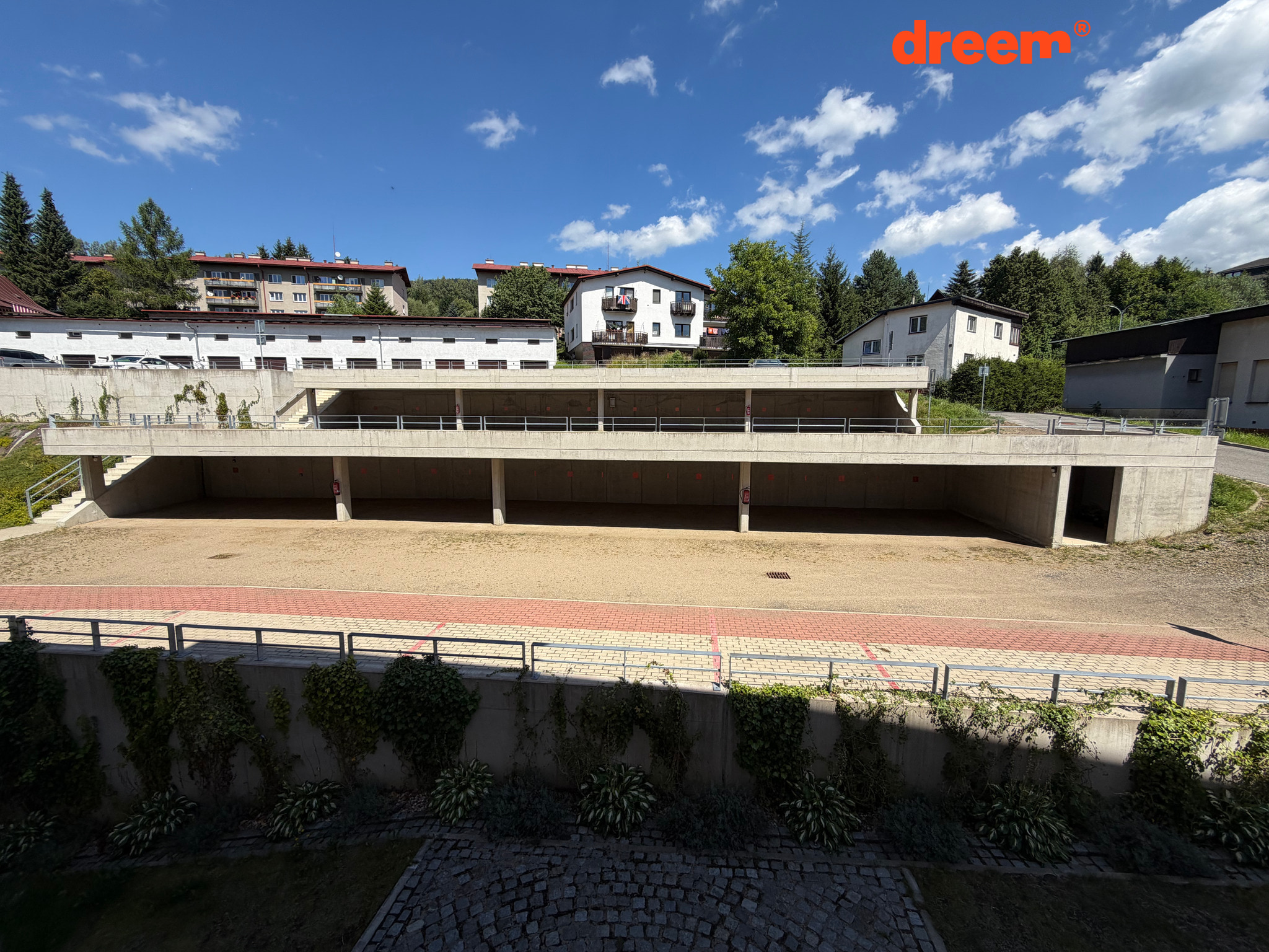 Pohled na dvoupodlažní betonovou konstrukci s krytými parkovacími místy za slunečného dne