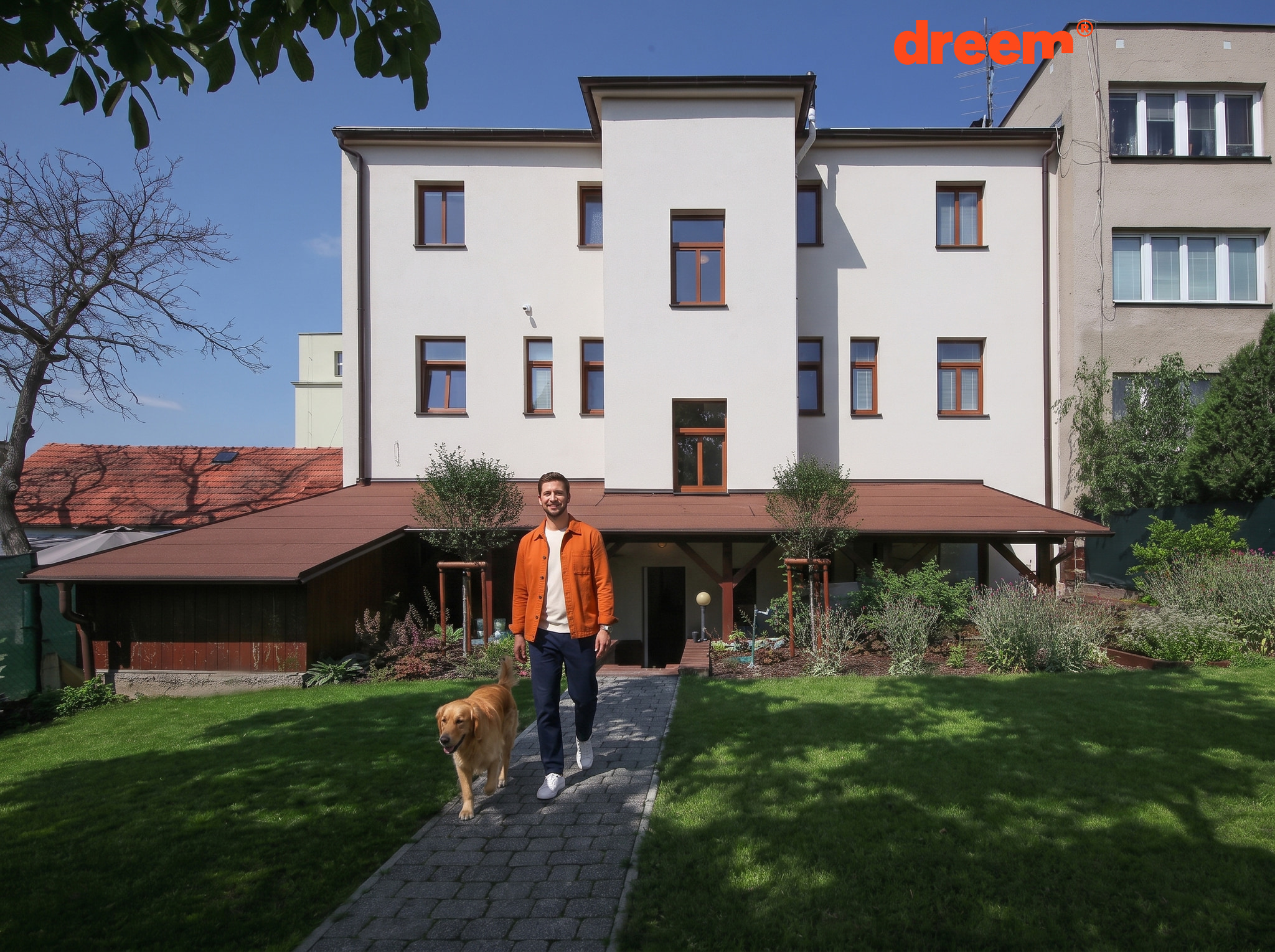 Vícepodlažní dům se světlou fasádou, dřevěnými okny a krytou terasou vedoucí do zatravněné zahrady s dlážděným chodníkem