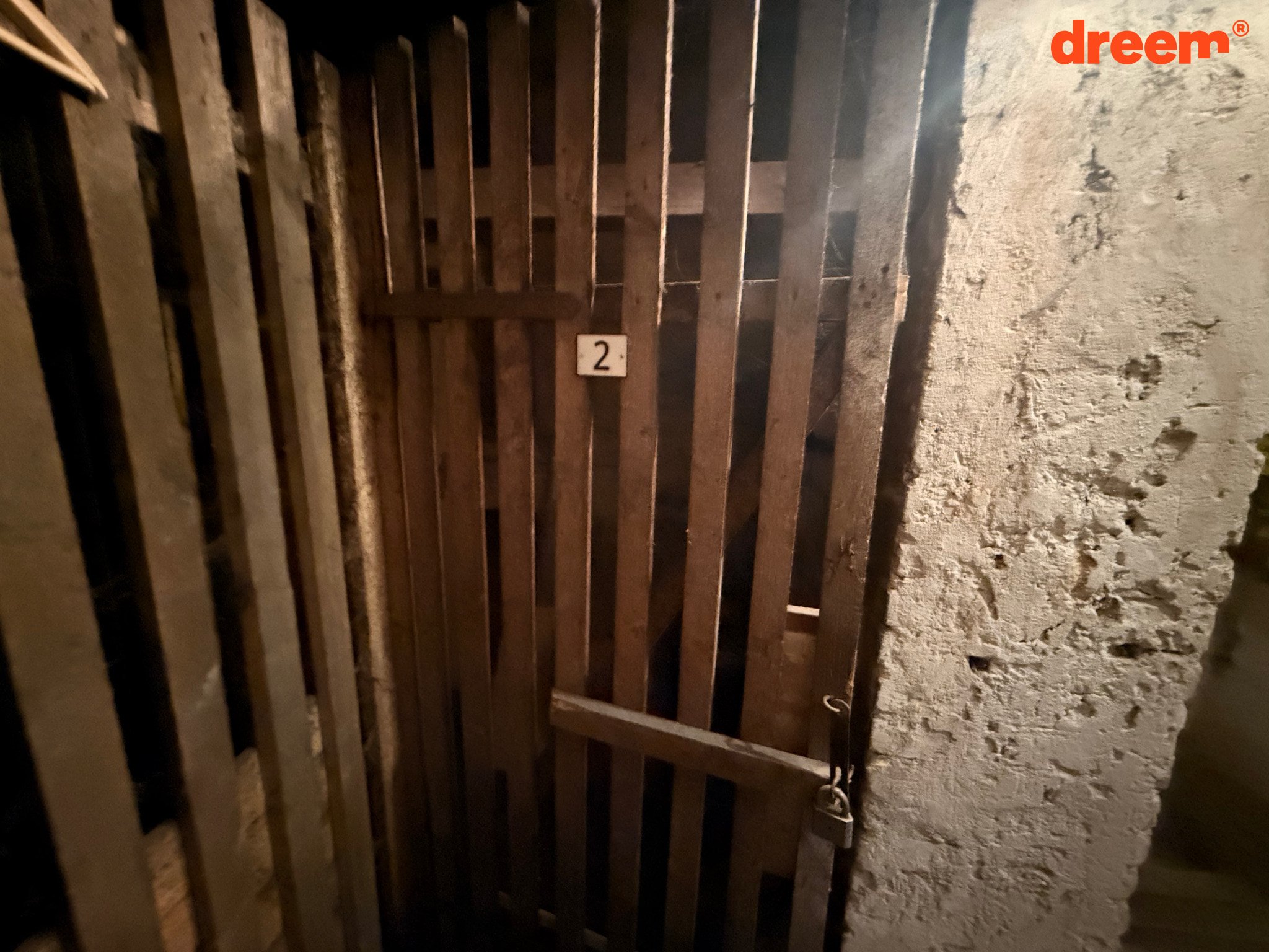 Uzamčená dřevěná laťková sklepní kóje s číslem dva vedle zděné stěny.