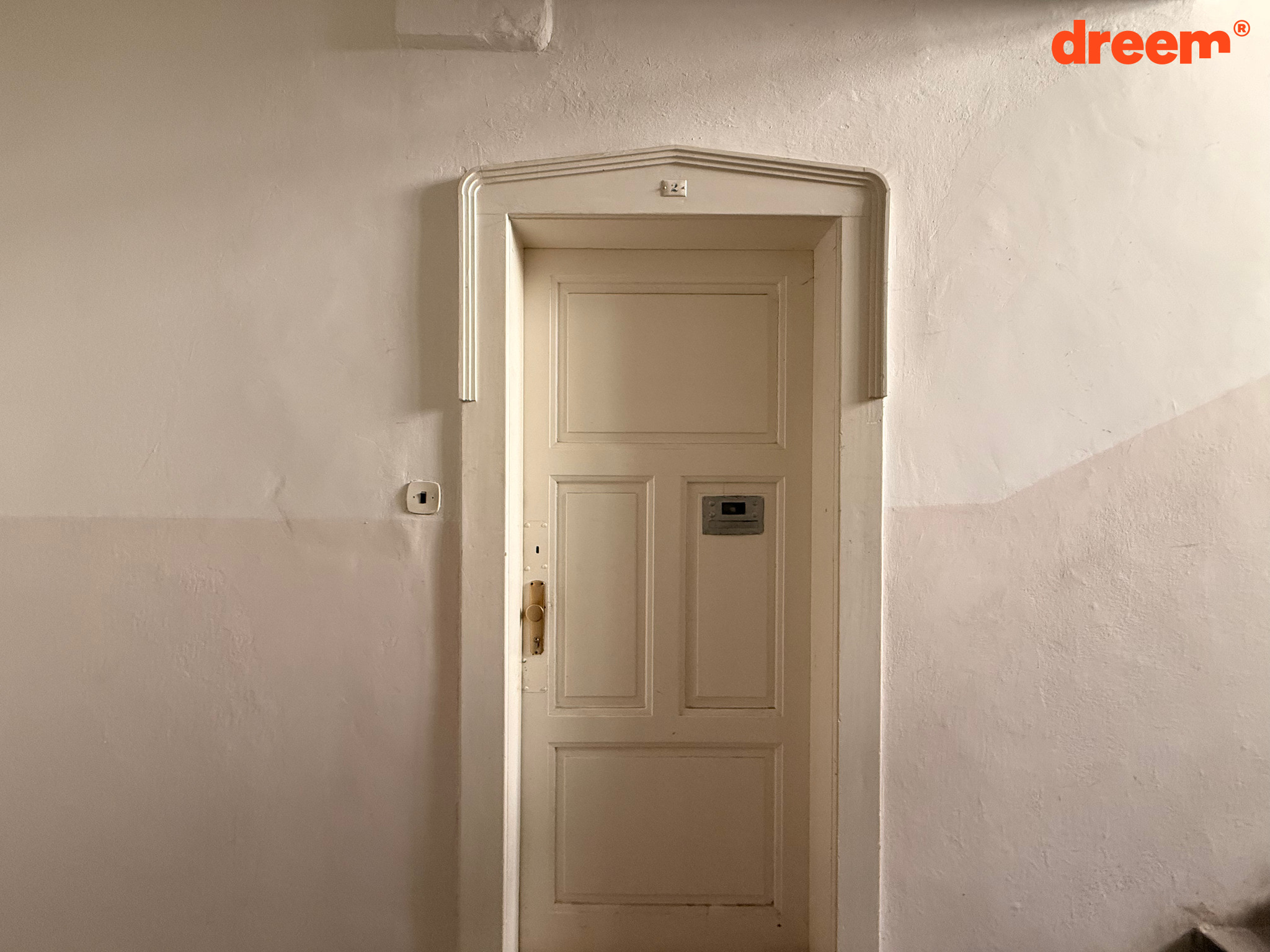 Bílé dřevěné vstupní dveře s ozdobným ostěním na společné chodbě domu.