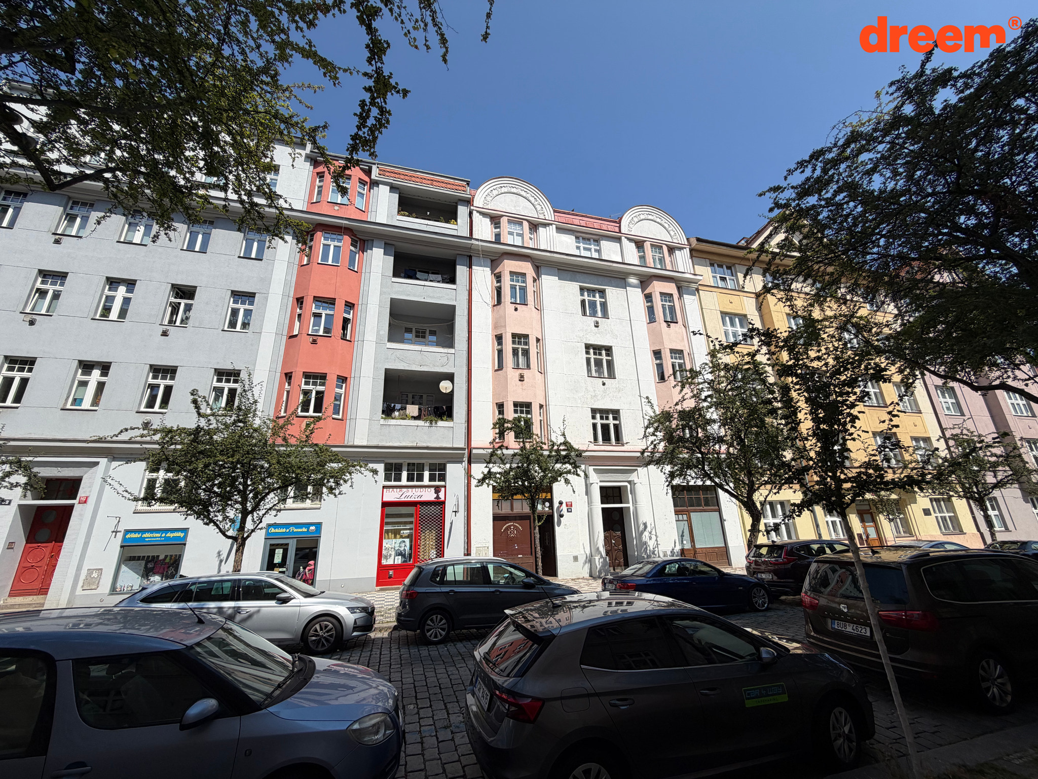 Záběr na řadu městských bytových domů s parkujícími auty v popředí za slunného dne